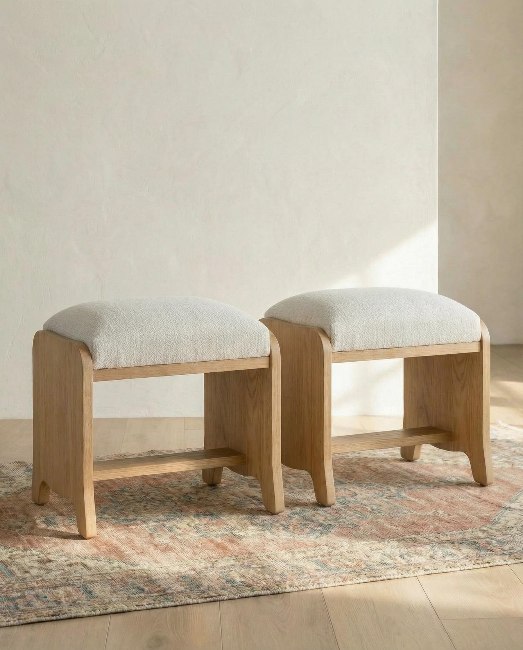 Two wooden stools with white cushioned seats on a patterned rug.
