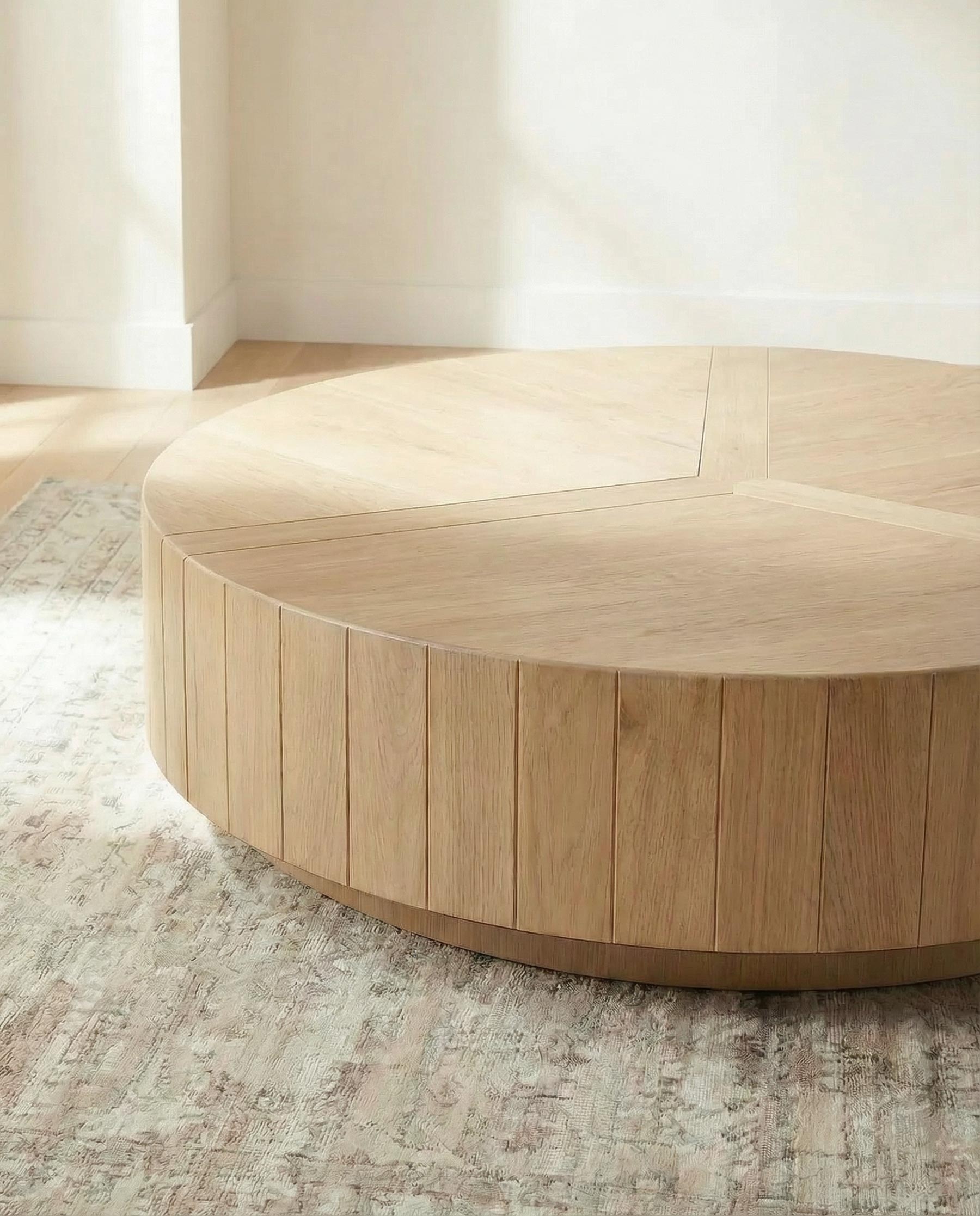 Round wooden coffee table in a minimalistic room with light-colored walls and floor.