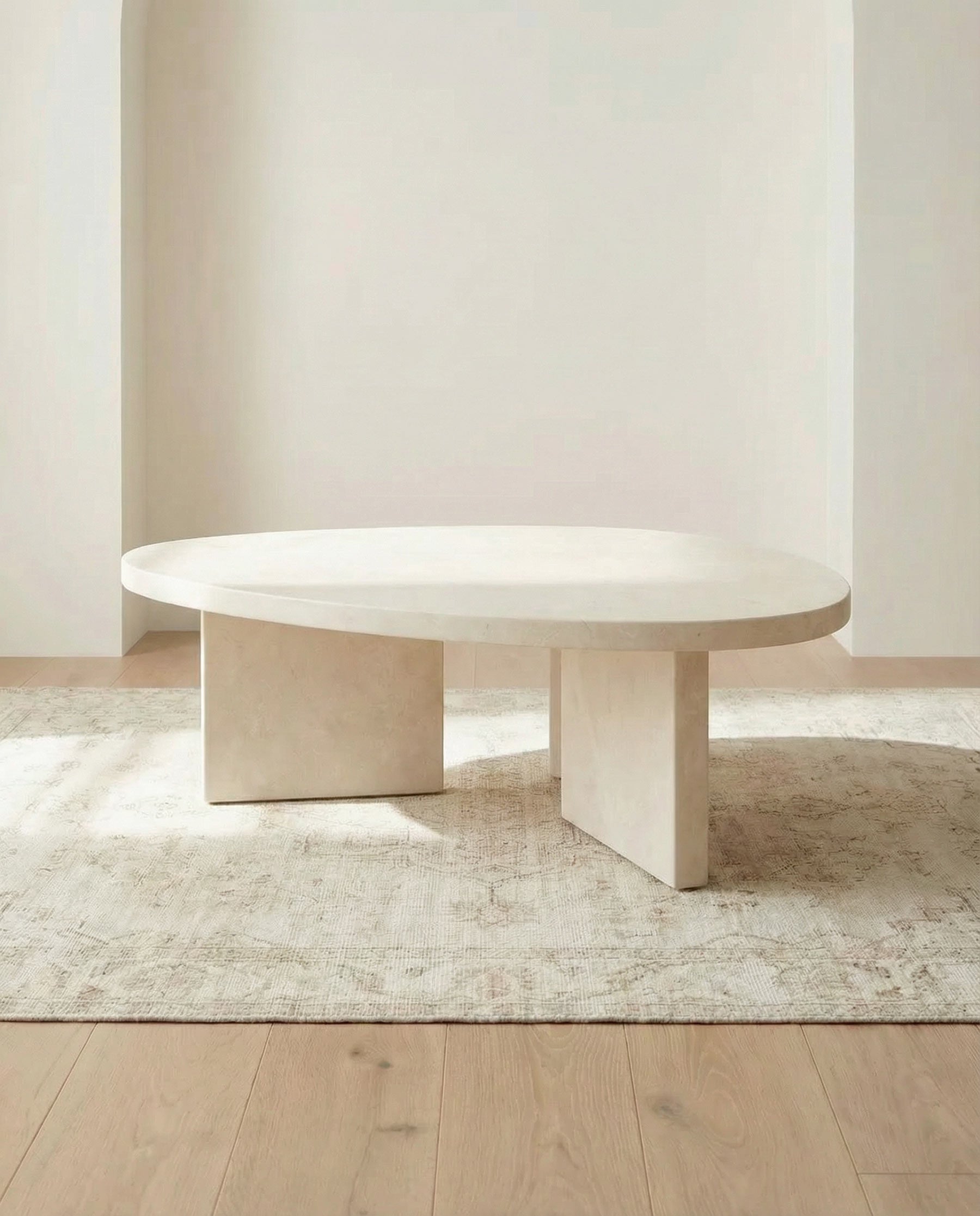 Round marble coffee table in a minimalistic room with light wood flooring and a plain wall.
