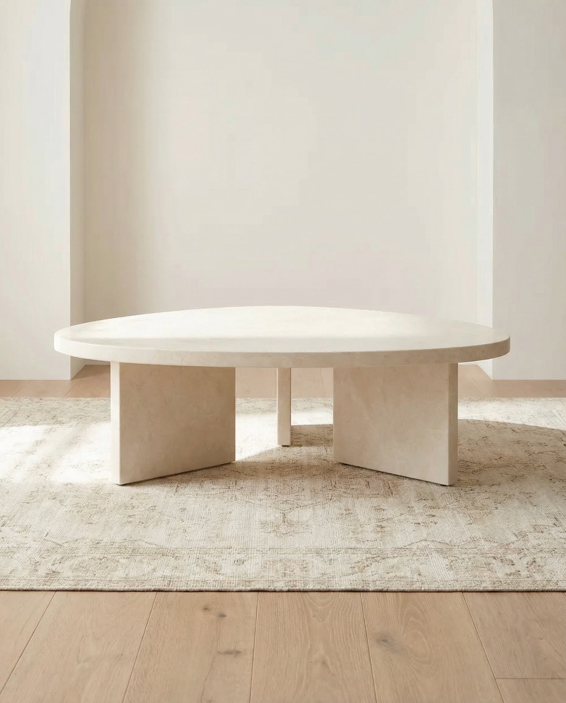 Beige stone dining table in a minimalistic room with light wood flooring and a neutral rug.