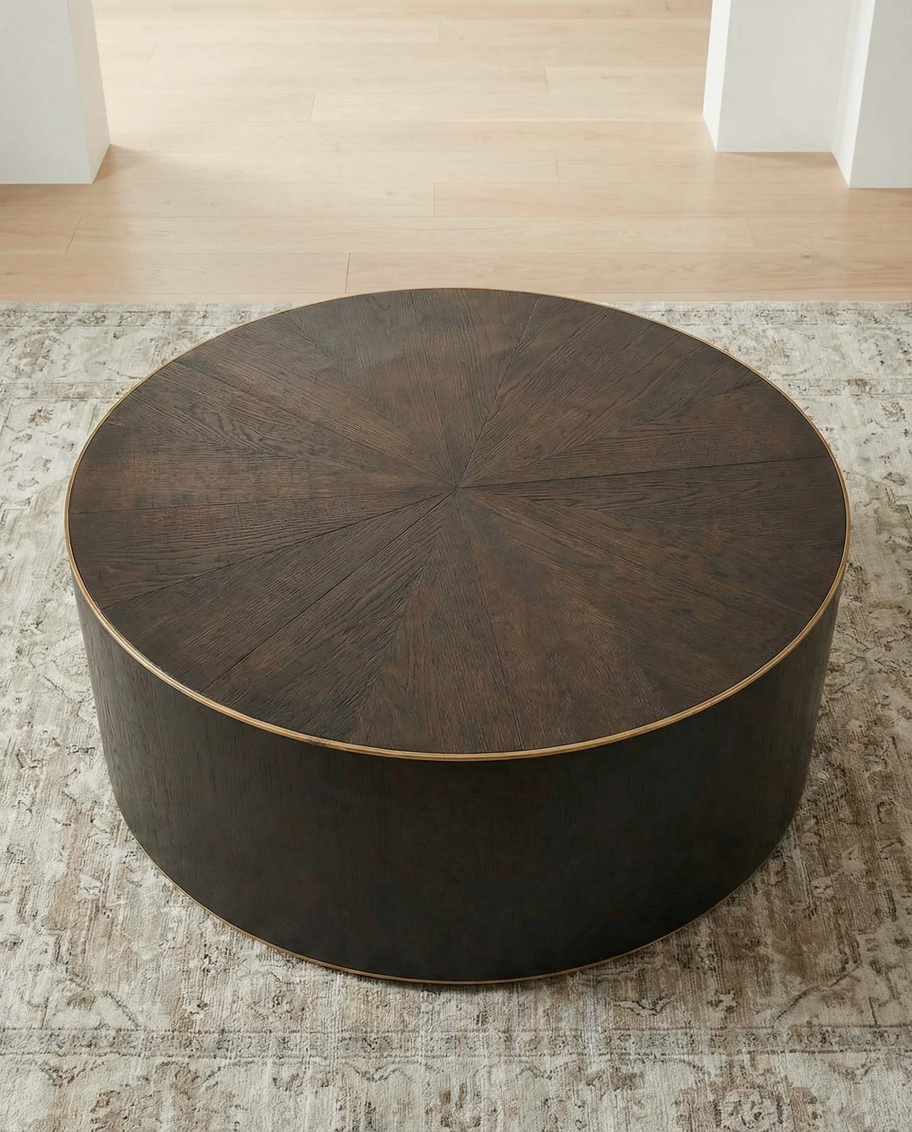 Round oak and brass coffee table on a textured rug with a light wood floor background