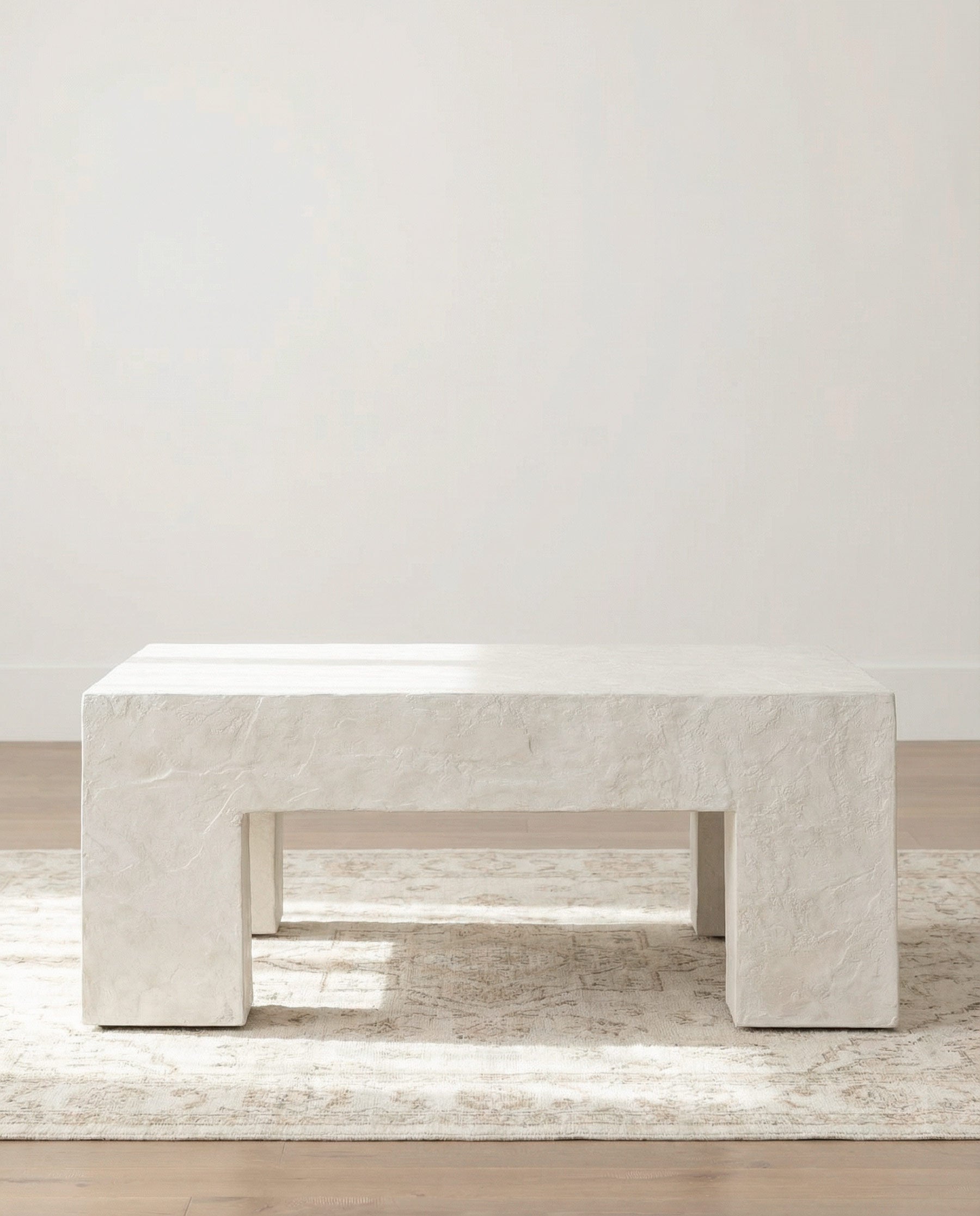 White plaster coffee table on a light wood floor with a white wall background