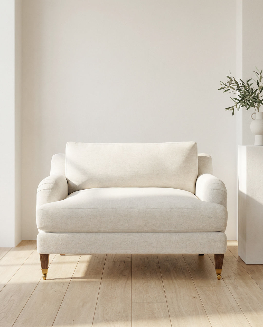 White armchair in a minimalistic room with a plant on a white wall.