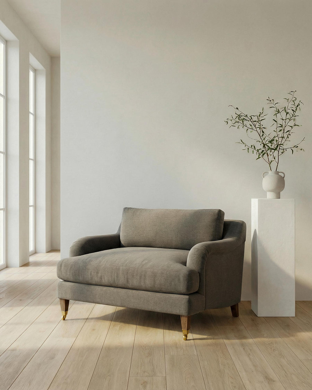 Gray armchair in a minimalistic room with a plant on a white pedestal.