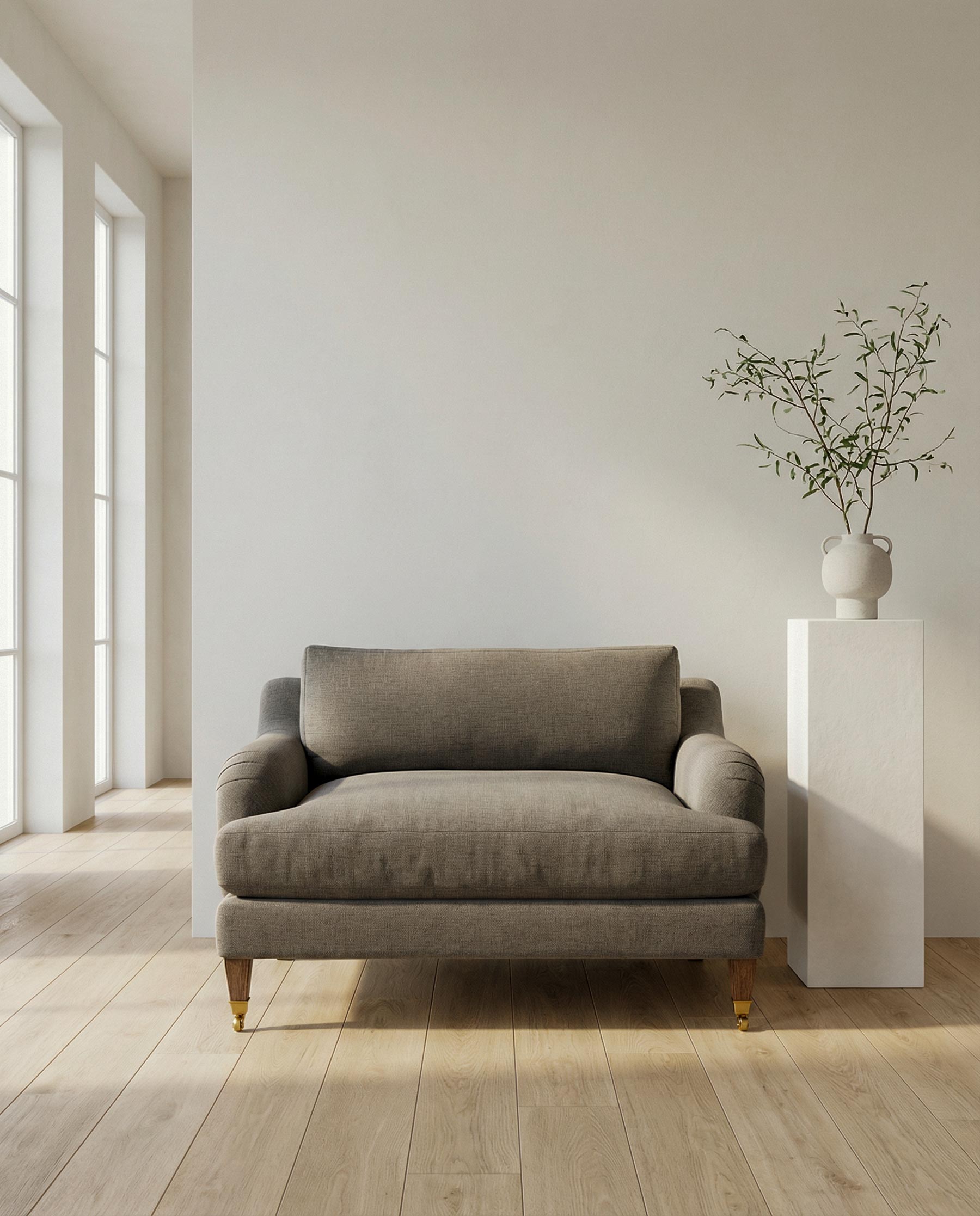 Gray lounge chair in a minimalistic room with a plant on a white pedestal.